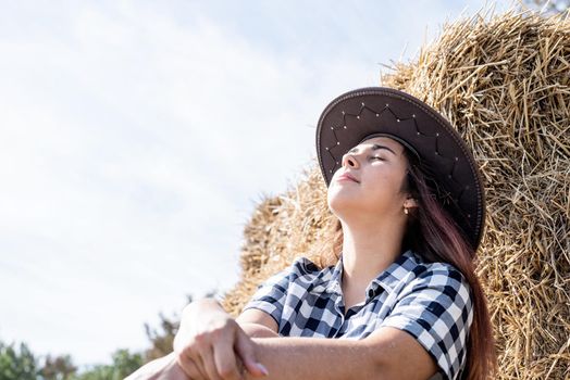 Beautiful girl on straw bales. beautiful woman in plaid shirt and cowboy hat resting on haystack