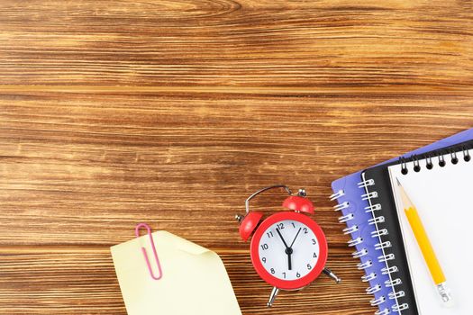 Spiral notebook with pencil and alarm clock on a wooden background. Flat lay. Back to school concept. Study desk.Top view.