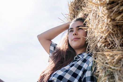 Beautiful girl on straw bales. beautiful woman in plaid shirt and cowboy hat resting on haystack