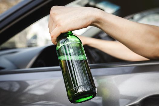 The driver's hand in the car window holds a bottle of alcohol.