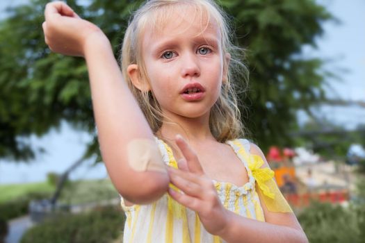 Close-up portrait of little girl. blonde, European appearance, summer day. the child fell in the park and injured his hand. Elbow injury, little girl crying. Tears on the face, pain, suffering, Summer