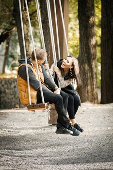 Vertical image of a happy couple in love on a swing in a forest park during the warm season. High quality photo