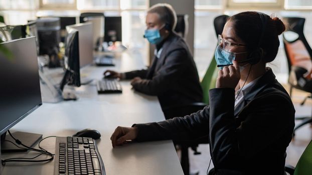 Two women in medical masks and headsets are working in the office.