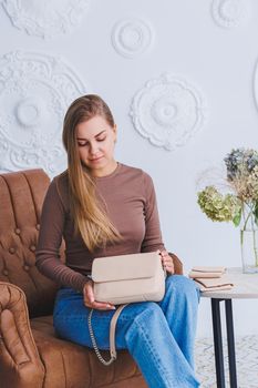 A beautiful woman holds a beige leather bag in her hands. A small women's cocktail bag.
