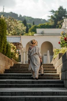 Woman on the stairs in the park. A middle-aged lady in a hat in a white outfit with a bag walks around the Livadia Palace.