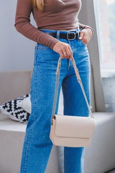 A beautiful woman holds a beige leather bag in her hands. A small women's cocktail bag.