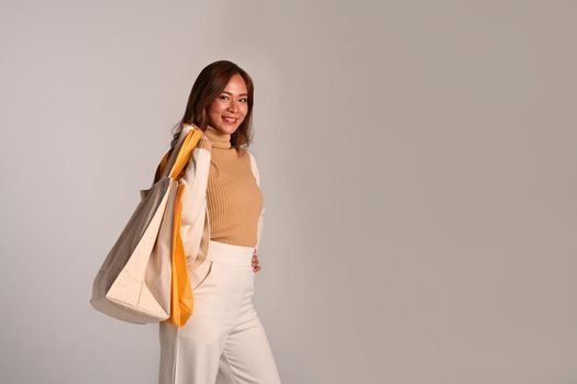 Portrait of beautiful woman carrying shopping bags standing on grey background. Black Friday, sale, shopping concept.