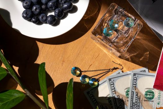 Blueberries in a white plate on a wooden table against the background of American dollars, magazines and plants with green leaves...