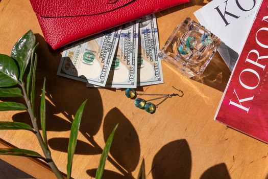 American dollars and a red genuine leather wallet on a wooden surface with fashion magazines and sunglasses.,,