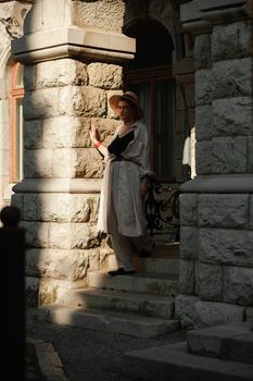 A woman in a hat in a white outfit with a bag walks around the Livadia Palace.