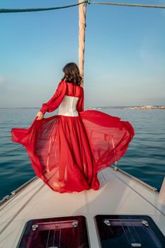 Attractive middle-aged woman in a red dress on a yacht on a summer day. Luxury summer adventure, outdoor activities