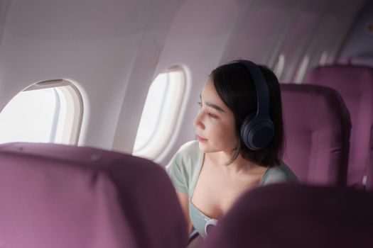 Young asian woman wear headphones for noise cancellation search songs in online shop on app during flight on board. Travel concept.