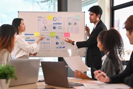 Young female employee and her colleague giving presenting new marketing strategy on flip chart at corporate meeting.