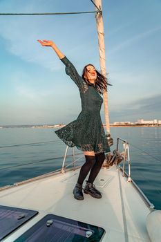 Woman standing on the nose of the yacht at a sunny summer day, breeze developing hair, beautiful sea on background.