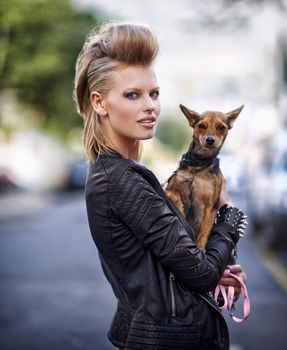Hes the perfect side-kick. A beautiful young trendy woman holding her small dog in a city street