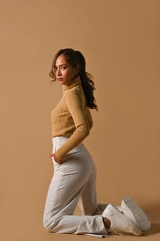 Confident fashionable woman wearing warm clothes posing isolated on beige background. Fashion, beauty concept.