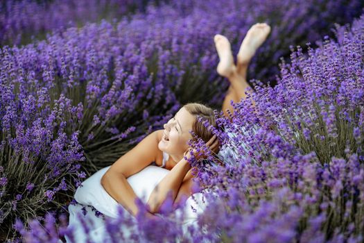 A middle-aged woman lies in a lavender field and enjoys aromatherapy. Aromatherapy concept, lavender oil, photo session in lavender.