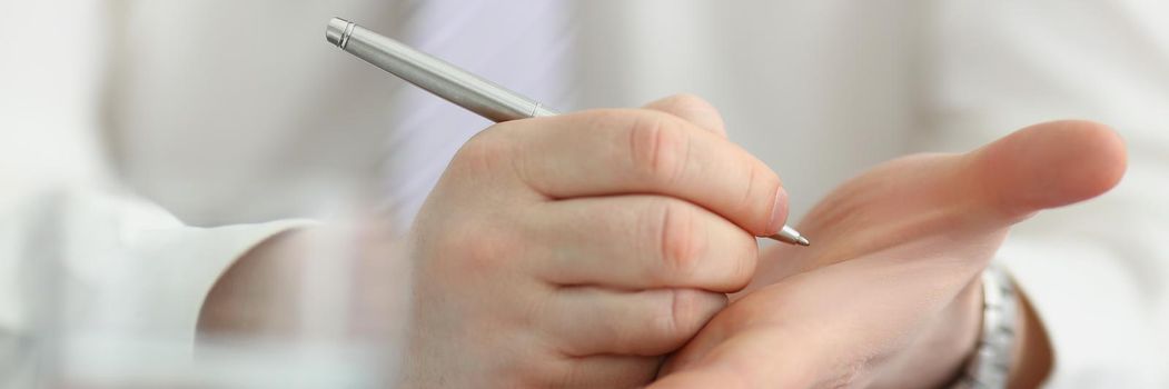 Close-up of male writing note with silver pen on his hand to keep in mind some information. Try not to forget, to do list, reminder. Note, memory concept