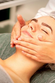 Beautiful caucasian young woman receiving a facial massage with closed eyes in spa salon, close up. Relaxing treatment concept