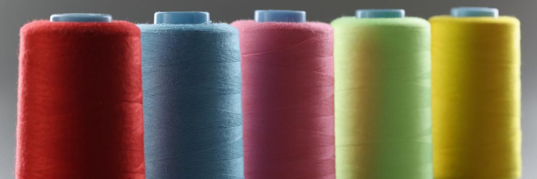 Close-up of group of whole haberdashery item colorful thread spools on grey surface. Colorful bobbins for tailoring. Dressmaking, atelier, fashion concept