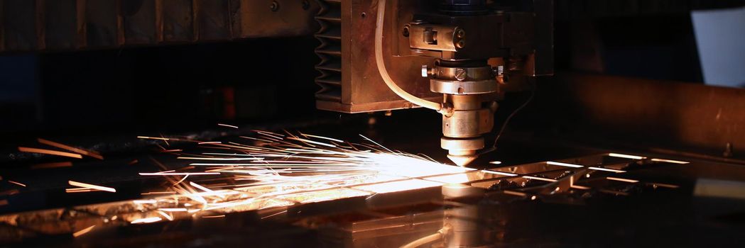 Close-up of sparks fly out of automated machine, metal processing laser on metallurgical background. Manufacturing, parts for automotive production concept
