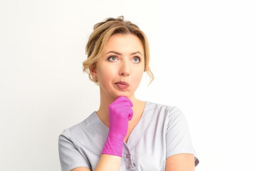 Young caucasian female doctor wearing gloves thoughtful looking away isolated on white background