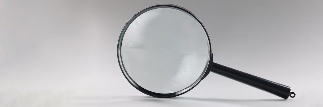 Close-up of single magnifying glass with black handle, leaning on grey surface. Simple design of lens or loupe to enlarge objects. Magnifying lens concept