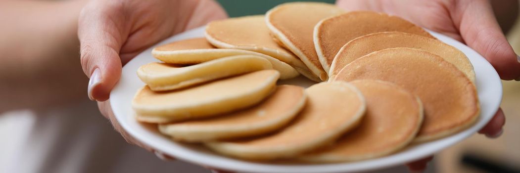 Close-up of woman holding plate with tasty fresh homemade pancakes. Hot delicious meal for breakfast, nutritious food to start day. Food, eating concept