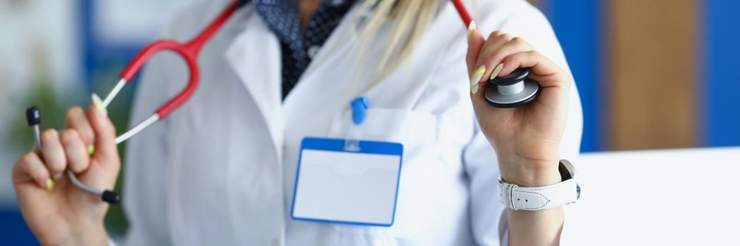 Close-up of female medical worker in white uniform posing with stethoscope on neck. Young woman specialist in office. Healthcare, appointment, help concept