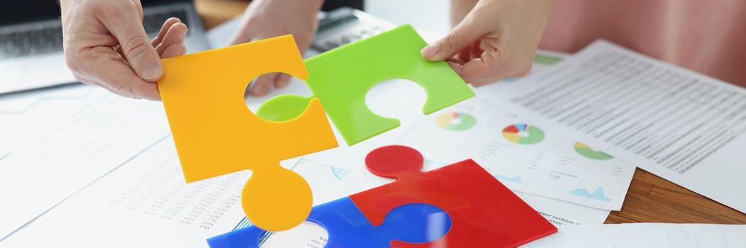 Close-up of coworkers solving jigsaw puzzle on workplace, colourful parts. Put puzzles into one, whole picture. New idea search, mind development concept