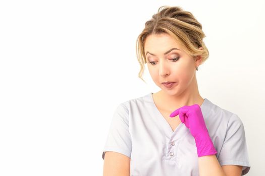 Young caucasian female doctor wearing gloves thoughtful looking down against a white background