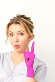 Young caucasian woman doctor wearing pink gloves keeping index finger pointed upwards making a gesture with index finger. I have an idea