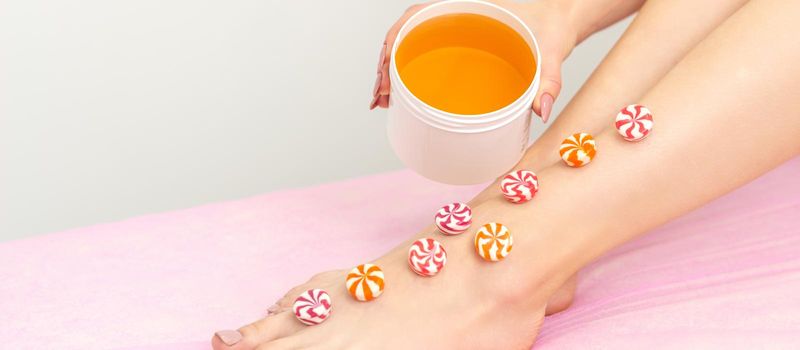 Depilation, waxing concept. Round candies lying down in a row on the female leg with a jar of sugar paste, close up