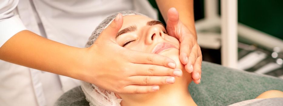 Facial treatment massage. Beautiful young caucasian woman with perfect skin receiving face and neck massage at a beauty spa