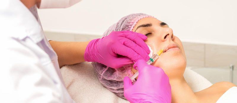 Young caucasian woman getting botox injection with hyaluronic acid in the lips at a beauty clinic