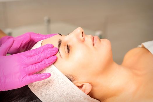 Cosmetologist with gloved hands applies a moisturizing mask with peeling cream on the female face. Facial cosmetology treatment. Procedures for facial care