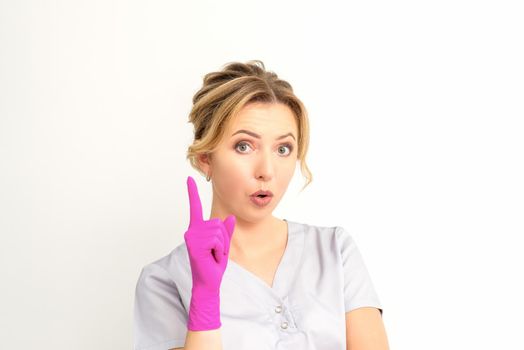 Young caucasian woman doctor wearing pink gloves keeping index finger pointed upwards making a gesture with index finger. I have an idea