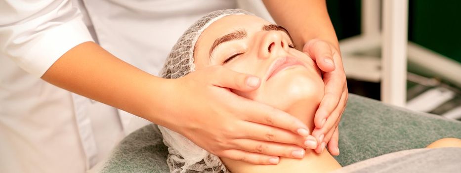Facial treatment massage. Beautiful young caucasian woman with perfect skin receiving face and neck massage at a beauty spa