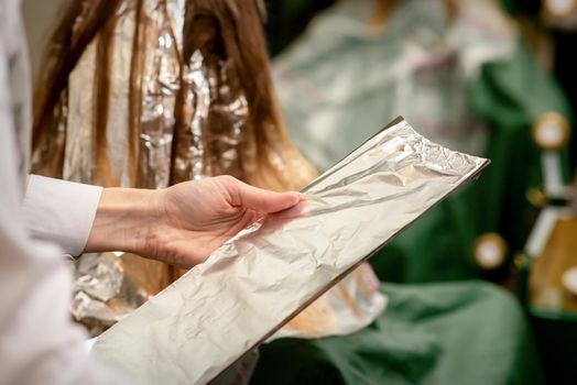 Hairdresser's Hands Holding Foil Sheet For Hair Dye In Beauty Salon
