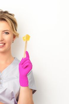 The master of sugar hair removal holds liquid yellow sugar paste, wax for depilation on a wooden stick on a white background