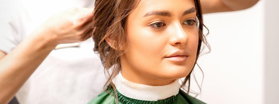 Hairstyling bride. A female hairdresser makes styling hair for the beautiful young caucasian woman in a beauty salon