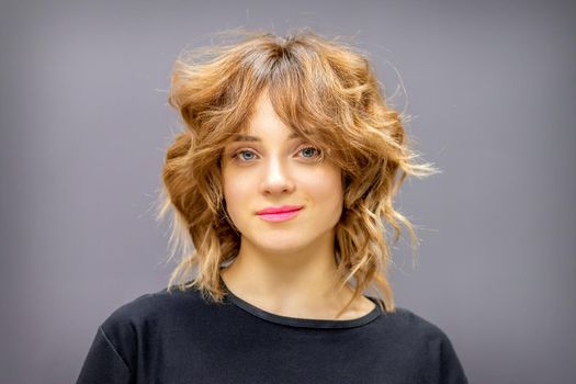 Portrait of a beautiful young caucasian red-haired woman with short wavy hairstyle smiling and looking at camera on dark gray background with copy space