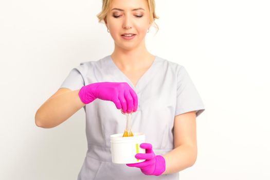 Portrait of a female caucasian beautician holding a jar of sugar paste for sugaring wearing pink gloves on white background