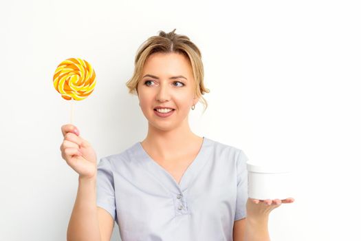Waxing, depilation concept. The beautician is wearing a medical coat holding a sugar lollipop with a jar of sugar paste on white background