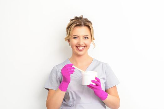 Portrait of a female caucasian beautician holding a jar of sugar paste for sugaring wearing pink gloves on white background