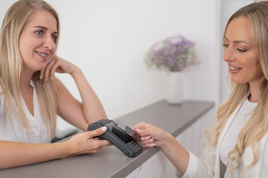 A young woman pays in a beauty salon with a credit card using NFC contactless payment