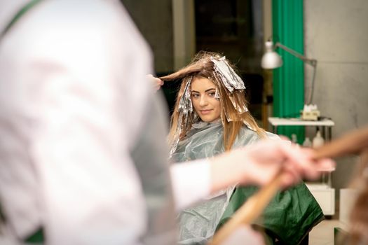 Portrait of a beautiful young caucasian woman who is smiling getting dyeing her hair with foil in a beauty salon