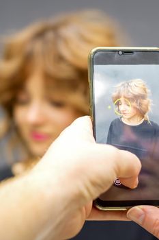 Man hairdresser taking pictures on the smartphone of her client's hairstyle against a gray background