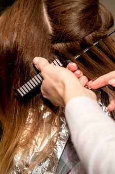 Hairdresser's hands prepare brown hair for dyeing with a comb and foil in a beauty salon, close up