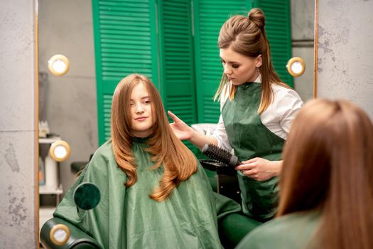 Professional hair care. Young female red-haired with long hair receiving hairstyling in a beauty salon.